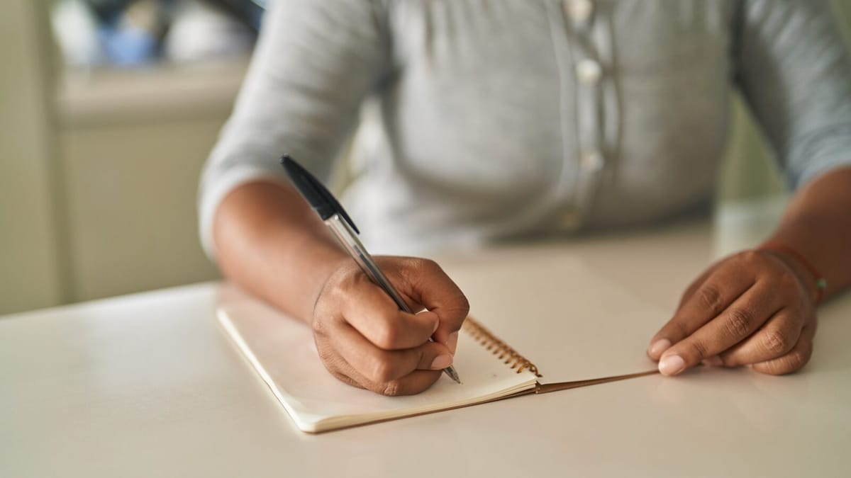 Mão de uma estudante escrevendo com caneta esferográfica preta em um caderno