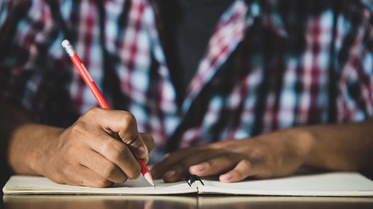Estudante escrevendo em um caderno aberto sobre a mesa