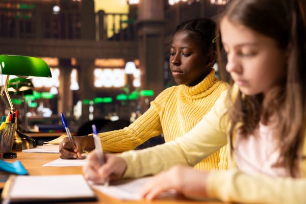 Estudantes estudando juntos em uma mesa de biblioteca com livros e cadernos